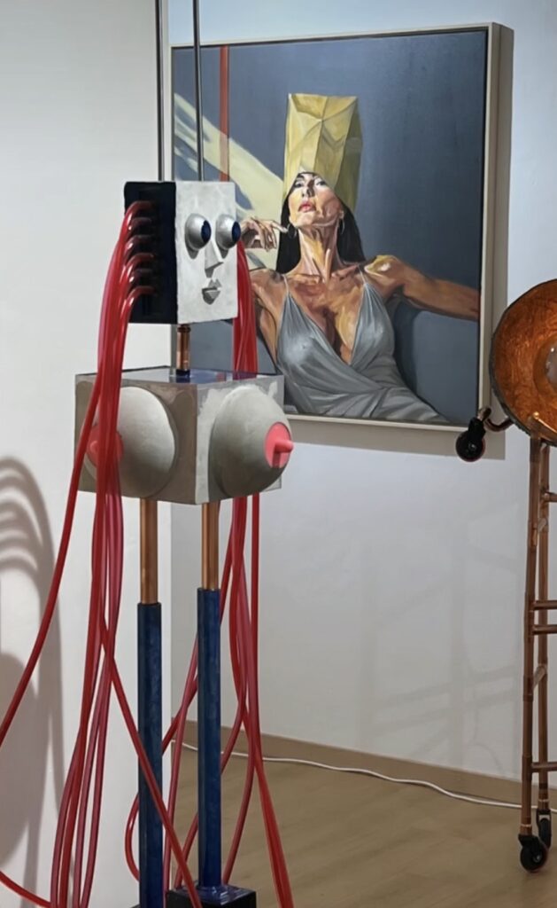 Sculpture with red cables in front of a painting of a woman with a paper bag over her head.